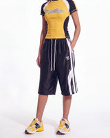 A model wearing a yellow, black, and white athletic top and matching black athletic shorts with white stripes and drawstrings, paired with yellow and white sneakers, against a plain white background.