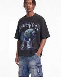 A man wearing a black Godspeed t-shirt with a large graphic of a planet and two seated figures, paired with blue denim cargo shorts, against a plain white background.