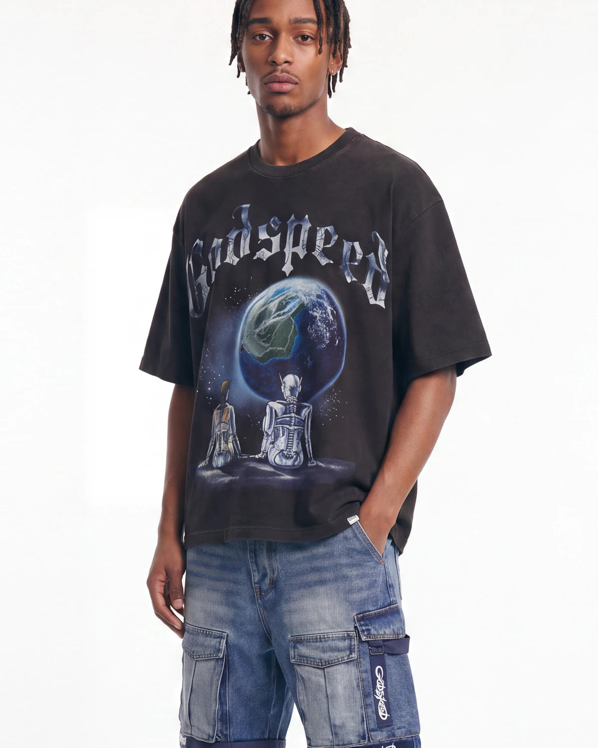 A man wearing a black Godspeed t-shirt with a large graphic of a planet and two seated figures, paired with blue denim cargo shorts, against a plain white background.