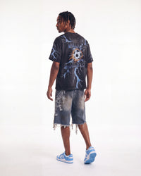 A man shown from the back wearing a black graphic t-shirt with a soccer ball and lightning design, matching acid-washed shorts, and blue and white sneakers, set against a plain white studio background.