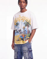 A man wearing a white graphic t-shirt with a colorful beach scene featuring a skeleton in a chair and the word 'Vendetta' in yellow, paired with blue denim cargo shorts.