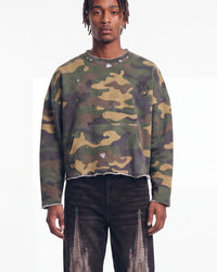 Saint Vanity Camo Crewneck in woodland camo, upper body front view on model showing the raw cut hem and paint splatter