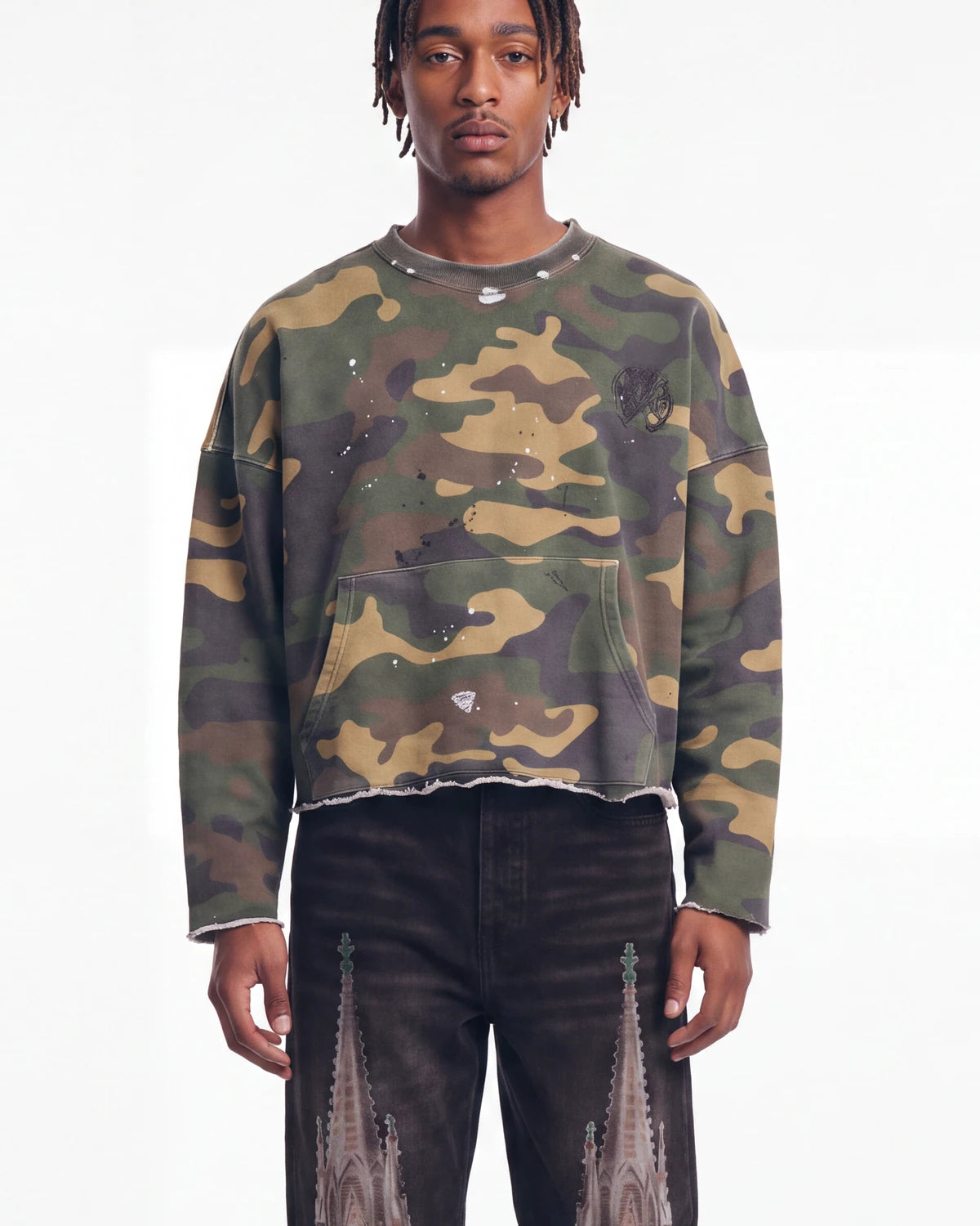 Saint Vanity Camo Crewneck in woodland camo, upper body front view on model showing the raw cut hem and paint splatter