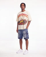 A man modeling a beige graphic t-shirt with a red and yellow 'TOO SLEEP' design, paired with blue denim cargo shorts and white sneakers, against a plain white studio background.