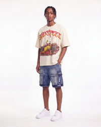 A man modeling a beige graphic t-shirt with a red and yellow 'TOO SLEEP' design, paired with blue denim cargo shorts and white sneakers, against a plain white studio background.