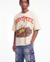 A man wearing a beige graphic t-shirt with a red and yellow 'SPEED' race car design, paired with blue cargo shorts, against a plain white background.
