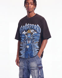 A man wearing a black Godspeed graphic t-shirt with a blue and white illustrated design, paired with blue denim cargo shorts, against a plain white background.