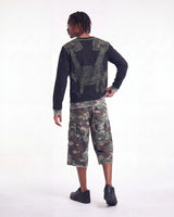A model shown from the back wearing a black long-sleeve shirt with a green tactical vest graphic on the back, paired with green and brown camouflage cargo shorts and black shoes, against a plain white studio background.