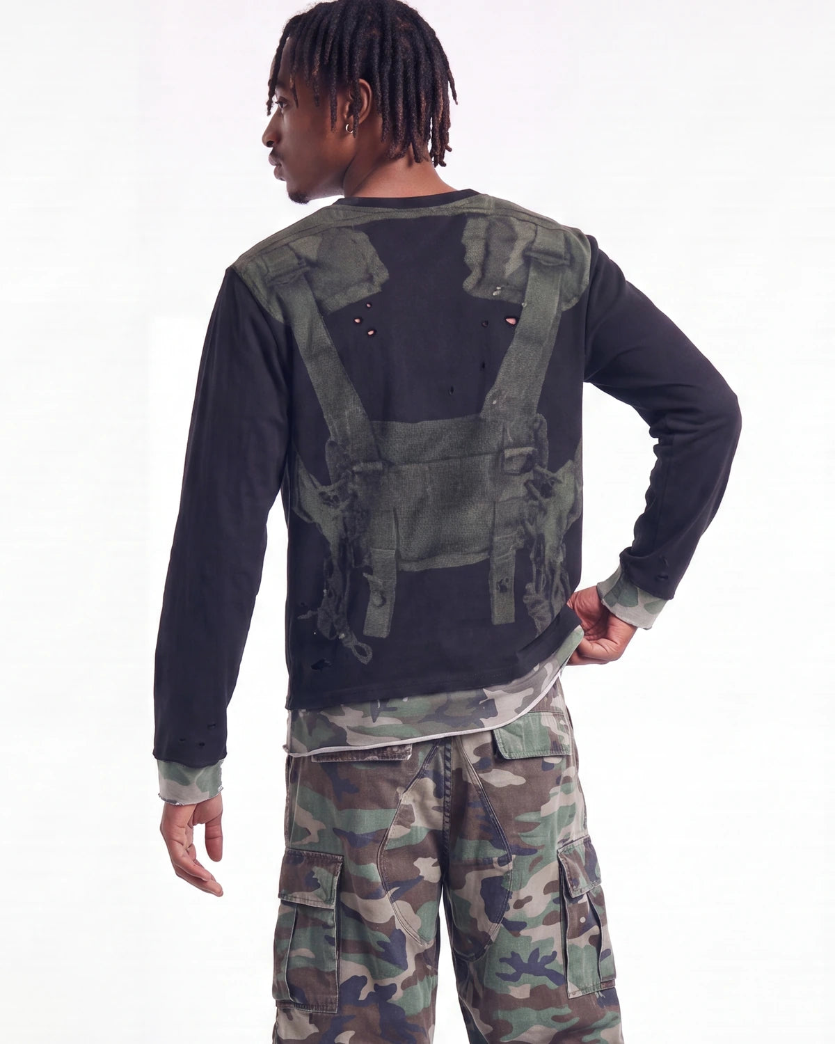 A man shown from the back wearing a black long-sleeve shirt with a distressed green tactical vest print, paired with green and brown camouflage cargo pants, against a plain white background.