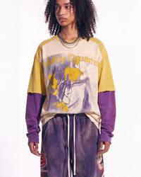 A model wearing a layered long-sleeve graphic t-shirt with a cream and yellow body, purple raglan sleeves, and a purple graphic print on the front reading 'Valley Dreams', paired with purple sweatpants against a white studio background.