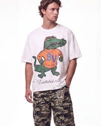 A man wearing a white graphic t-shirt with a green alligator mascot wearing an orange shirt with blue 'SV' lettering, paired with camouflage cargo pants, against a plain white background.