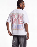 A man shown from the back wearing a white graphic t-shirt with a large distressed text print on the back reading 'EXCUSE ME I DON'T LIKE YOU' in pink and blue, paired with dark gray jeans against a white studio background.