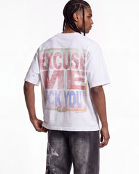A man shown from the back wearing a white graphic t-shirt with a large distressed text print on the back reading 'EXCUSE ME I DON'T LIKE YOU' in pink and blue, paired with dark gray jeans against a white studio background.