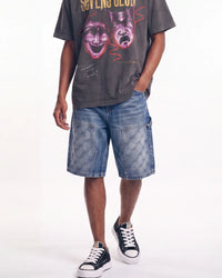 A model wearing a dark gray graphic t-shirt, blue denim shorts with a geometric pattern, and black canvas sneakers, shown from the waist down against a white studio background.