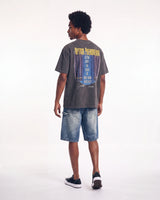 A man shown from the back wearing a faded dark gray graphic t-shirt with a blue and yellow print, paired with blue denim shorts and black sneakers, against a plain white studio background.