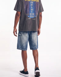 A model from the back wearing a faded black graphic t-shirt, blue denim shorts, and black low-top sneakers with white soles, set against a plain white studio background.