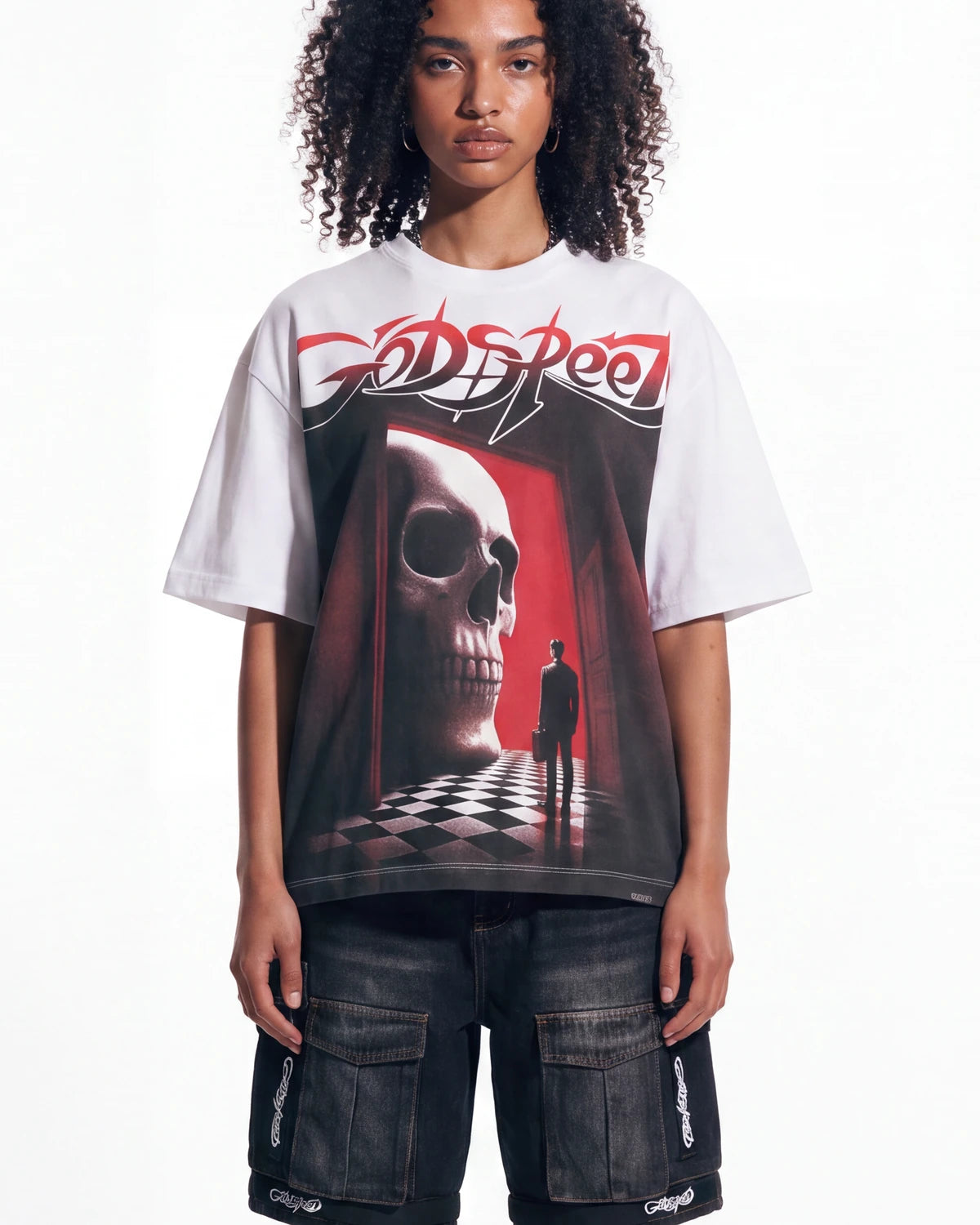 A model wearing a white Godspeed t-shirt with a large red, black, and white graphic print of a skull and a figure in a corridor, paired with dark cargo shorts.