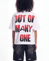 A person shown from the back wearing a white oversized T-shirt with large text reading 'OUT OF MANY, ONE' in black with a red gradient, paired with dark cargo shorts.