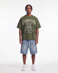 Godspeed Collegiate Tee Olive Wash, worn by a model with light wash denim shorts, full front view