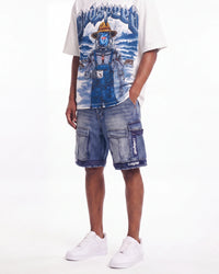 A model wearing a white graphic t-shirt with a blue robot print, blue denim cargo shorts with 'Cruze' branding on the pocket, and white sneakers, shown from the waist down against a white studio background.