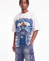 A model wearing a white graphic t-shirt featuring a blue and yellow 'Blindspot' character design, paired with blue denim cargo pants, against a plain white studio background.