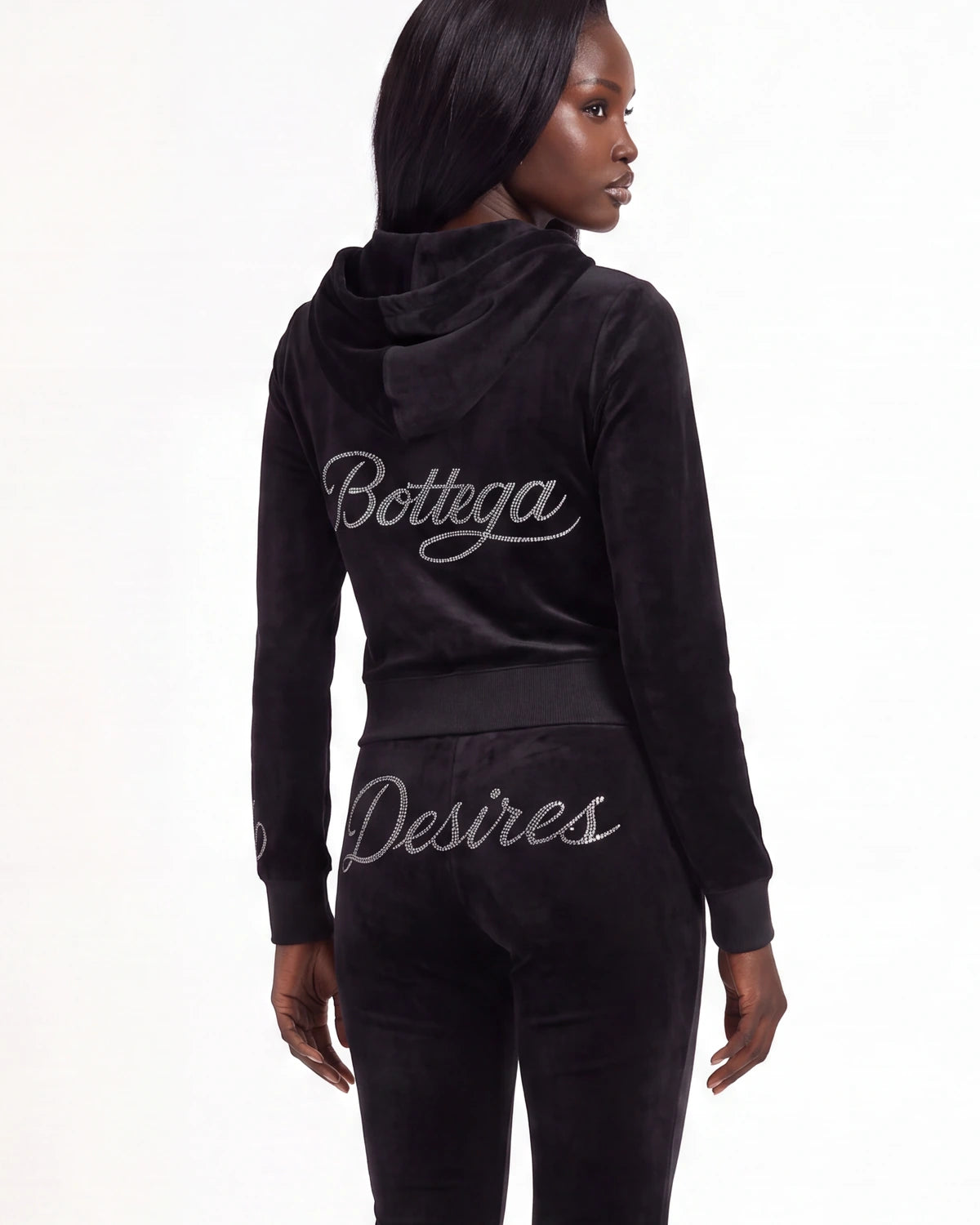 A model shown from the back wearing a black velour tracksuit with 'Bottega' and 'Desires' written in silver script across the back, against a plain white background.