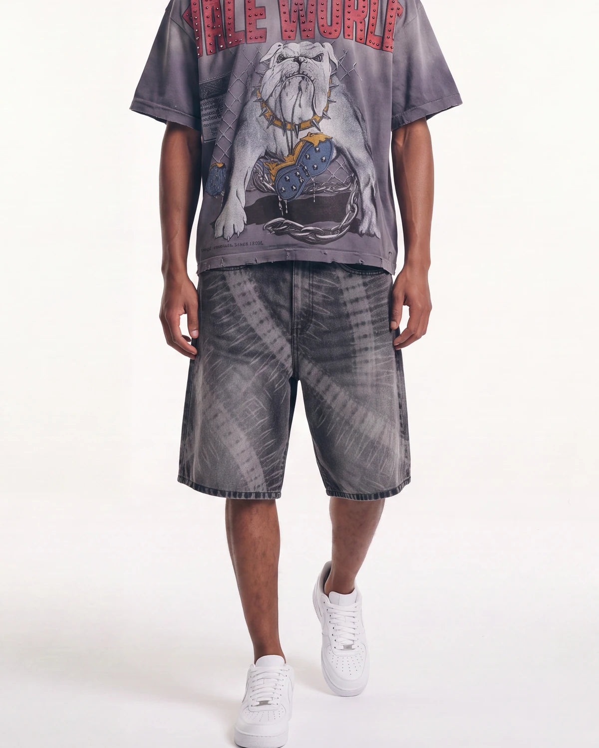 A model wearing a gray acid-wash graphic t-shirt with a bulldog print and red text, matching acid-wash shorts, and white sneakers, shown from the chest down against a white studio background.