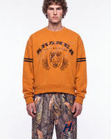 Sp5der Aranea Crewneck burnt orange, upper body front view on model showing the ARANEA crest graphic