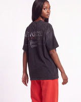 A woman shown from the back wearing a faded black graphic t-shirt and bright red sweatpants against a plain white studio background.