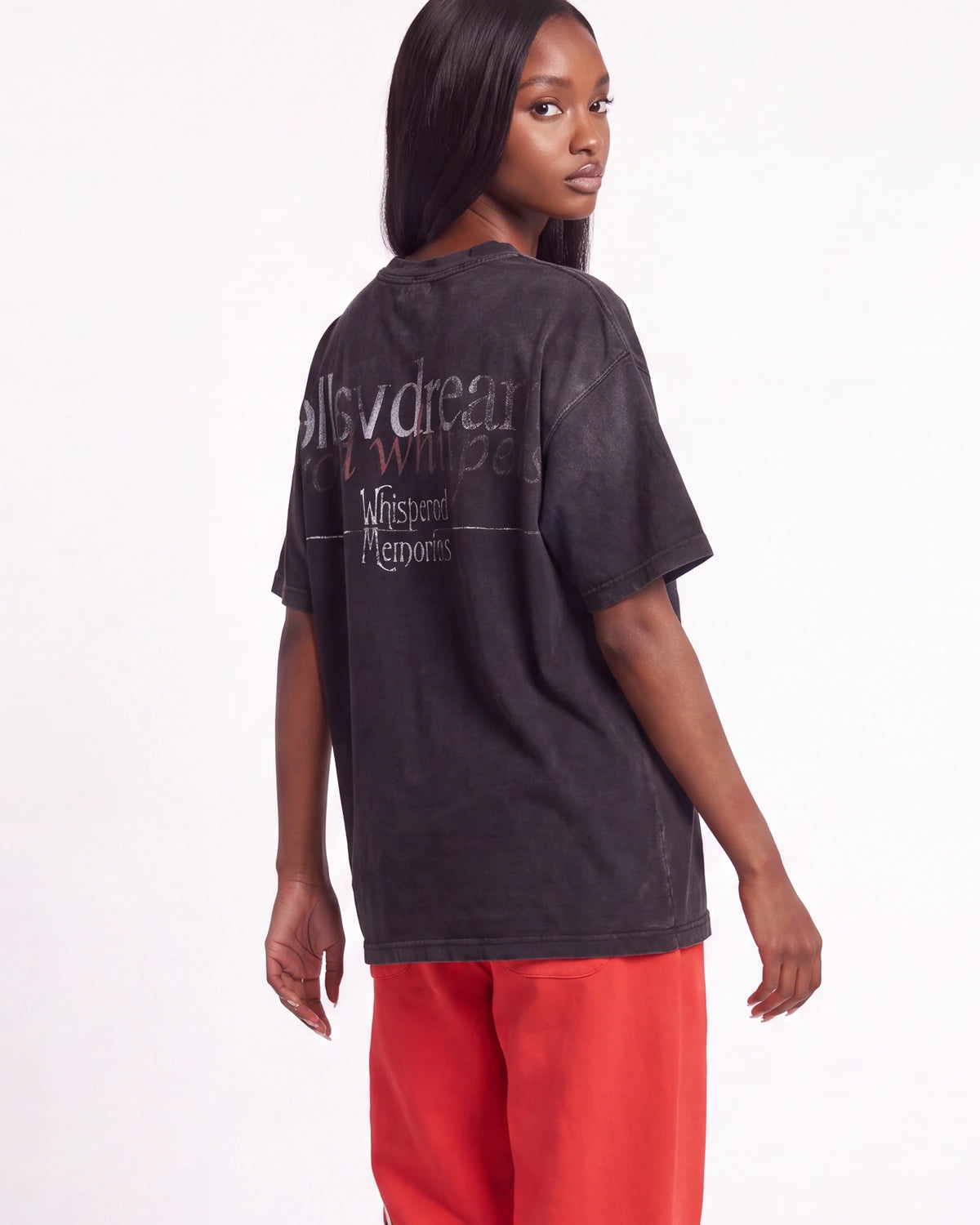 A woman shown from the back wearing a faded black graphic t-shirt and bright red sweatpants against a plain white studio background.