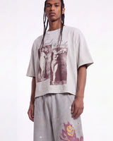 A model wearing a light gray oversized graphic t-shirt with a dark red print of two figures and the text 'Saint Security', paired with matching light gray sweatpants against a white studio background.