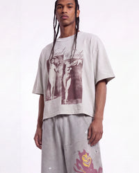A model wearing a light gray oversized graphic t-shirt with a dark red print of two figures and the text 'Saint Security', paired with matching light gray sweatpants against a white studio background.
