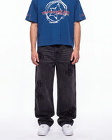 A model wearing a blue short-sleeve t-shirt with a white and red 'CHIMERA' graphic on the chest, paired with dark gray wide-leg jeans featuring black 'CHIMERA' embroidery on the legs, and white sneakers, against a plain white background.