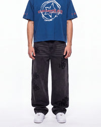 A model wearing a blue short-sleeve t-shirt with a white and red 'CHIMERA' graphic on the chest, paired with dark gray wide-leg jeans featuring black 'CHIMERA' embroidery on the legs, and white sneakers, against a plain white background.