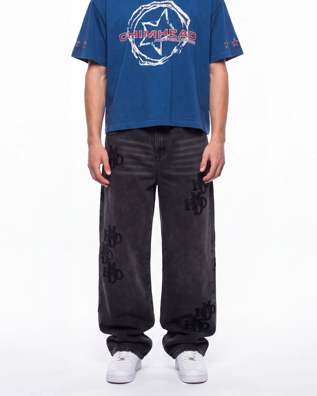 A model wearing a blue short-sleeve t-shirt with a white and red 'CHIMERA' graphic on the chest, paired with dark gray wide-leg jeans featuring black 'CHIMERA' embroidery on the legs, and white sneakers, against a plain white background.