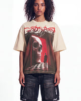 A model wearing a beige Godspeed t-shirt with a large red and black graphic print of a skull in a hallway, paired with dark cargo shorts, against a plain white background.
