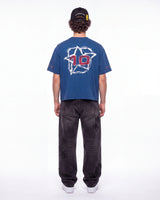 A person shown from the back wearing a blue short-sleeve T-shirt with a large white star graphic and red number 10 on the back, paired with dark gray jeans and a black cap, against a plain white studio background.