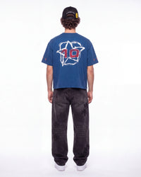 A person shown from the back wearing a blue short-sleeve T-shirt with a large white star graphic and red number 10 on the back, paired with dark gray jeans and a black cap, against a plain white studio background.