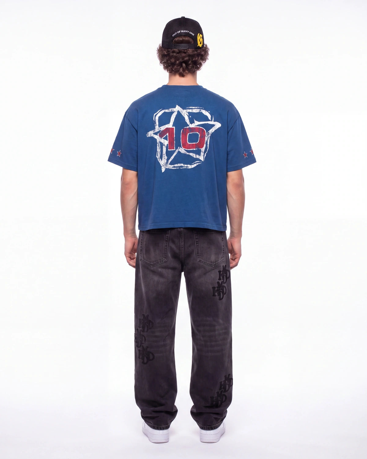 A person shown from the back wearing a blue short-sleeve T-shirt with a large white star graphic and red number 10 on the back, paired with dark gray jeans and a black cap, against a plain white studio background.
