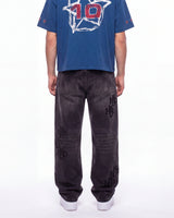 A person shown from the back wearing a blue graphic T-shirt with a large white and red '10' design, paired with dark gray washed jeans featuring black embroidered 'HO' logos on the legs, and white sneakers, against a plain white studio background.
