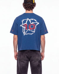 A person shown from the back wearing a blue cropped T-shirt with a large white outlined star graphic and red number 10 on the back, paired with dark jeans against a plain white studio background.