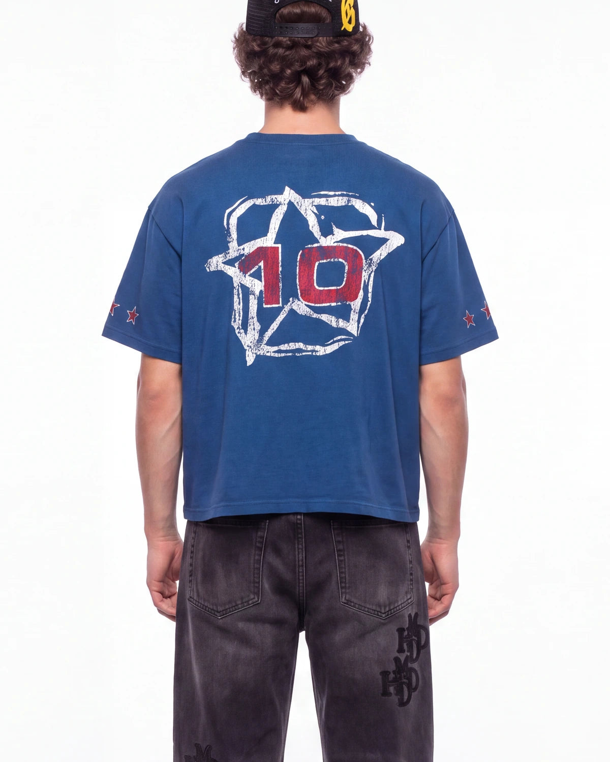 A person shown from the back wearing a blue cropped T-shirt with a large white outlined star graphic and red number 10 on the back, paired with dark jeans against a plain white studio background.