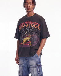 A man wearing a faded black Godspeed graphic t-shirt and blue cargo shorts, standing against a plain white studio background.