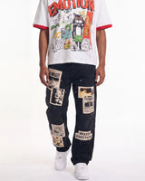 A model wearing a white graphic t-shirt with red trim and a black denim jacket covered in vintage-style newspaper clippings and patches, paired with white sneakers, against a plain white background.