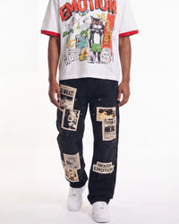 A model wearing a white graphic t-shirt with red trim and a black denim jacket covered in vintage-style newspaper clippings and patches, paired with white sneakers, against a plain white background.