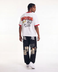 A model shown from the back wearing a white ringer t-shirt with red trim and a large graphic print on the back, paired with black graphic cargo pants and white sneakers, against a plain white studio background.