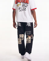 A person shown from the chest down wearing a white ringer T-shirt with red trim and a large graphic print, paired with black patchwork cargo pants and white sneakers, against a plain white studio background.