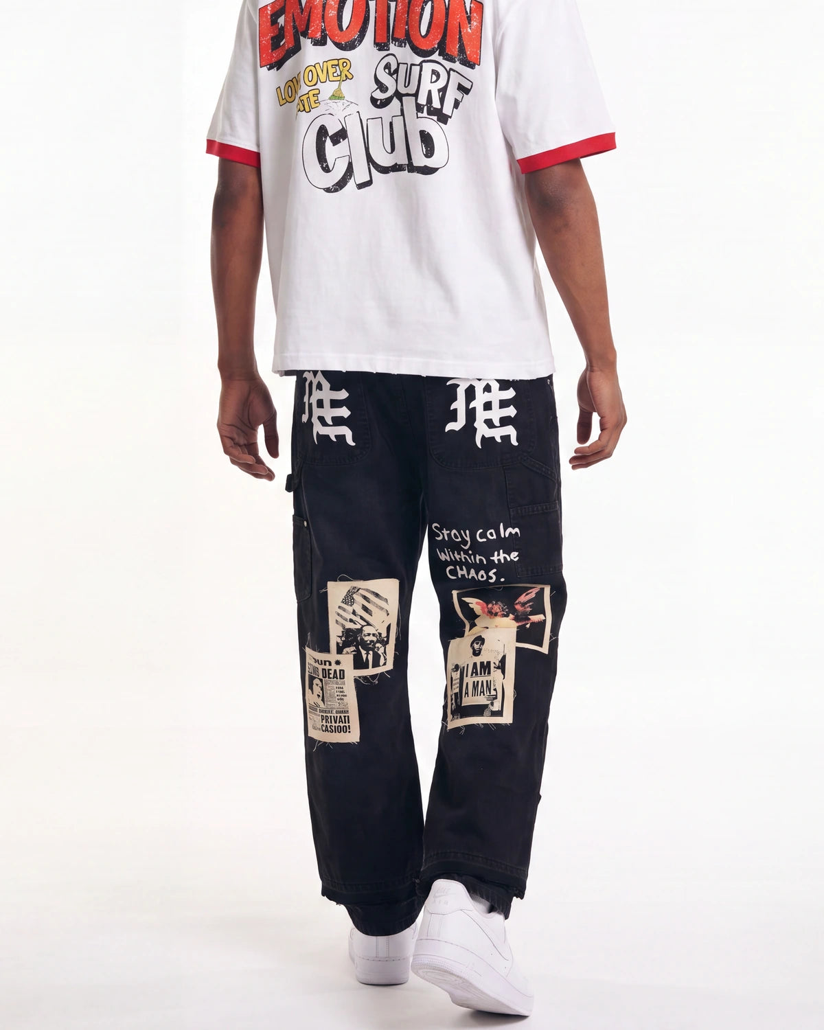 A person shown from the chest down wearing a white ringer T-shirt with red trim and a large graphic print, paired with black patchwork cargo pants and white sneakers, against a plain white studio background.
