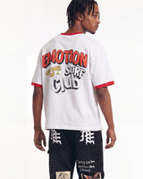 A man shown from the back wearing a white ringer t-shirt with red trim and a large graphic on the back that reads 'EMOTION SURF CLUB'. He is also wearing black graphic cargo pants.