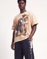 A male model wearing a beige graphic t-shirt with a bulldog weightlifting print and dark navy athletic pants with 'XSPORT' written vertically on the side, set against a plain white studio background.